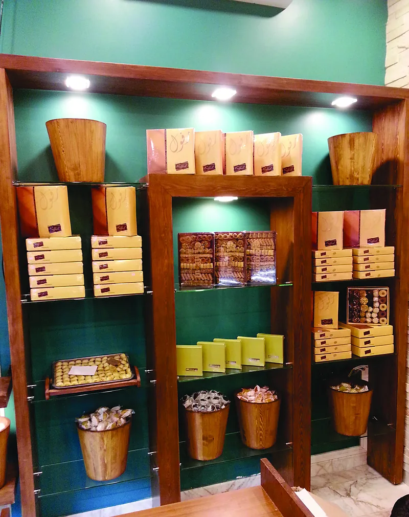 Étagères de présentation en bois sur fond vert, dans une chocolaterie-pâtisserie