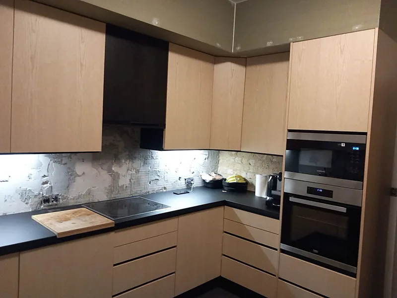 Cuisine d'angle sur mesure aux façades en bois clair, avec plan de travail noir et colonne de fours