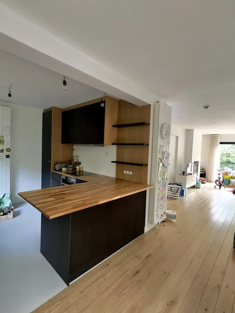 Cuisine sur mesure en chêne et panneaux noirs avec plan de travail en bois, ouverte sur le séjour