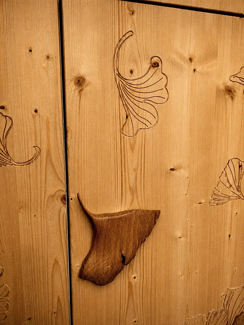 Poignée en bois sculptée à la main, entre deux portes de cuisine gravées de feuilles de ginkgo