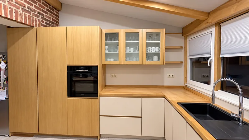 Cuisine en bois clair et façades crème : colonnes avec four, meubles hauts vitrés et plan de travail en bois