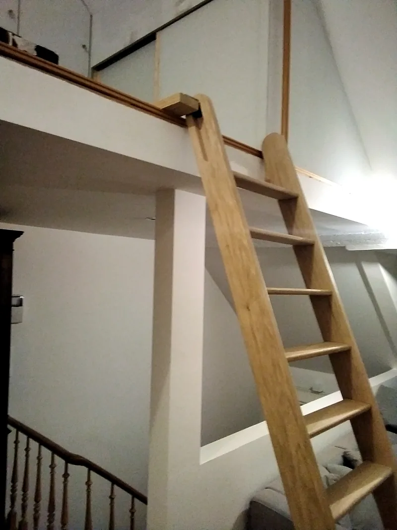 Échelle de meunier en bois vue de près, accrochée au garde-corps de la mezzanine