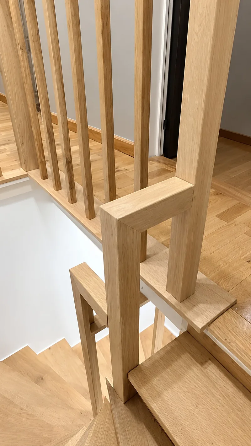Haut d'un escalier balancé en bois clair : poteau et main courante du garde-corps