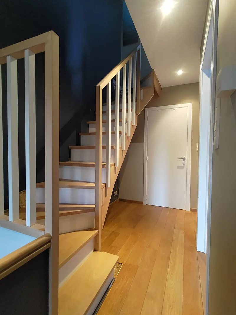 Escalier en bois avec garde-corps à barreaux blancs, vu depuis le couloir