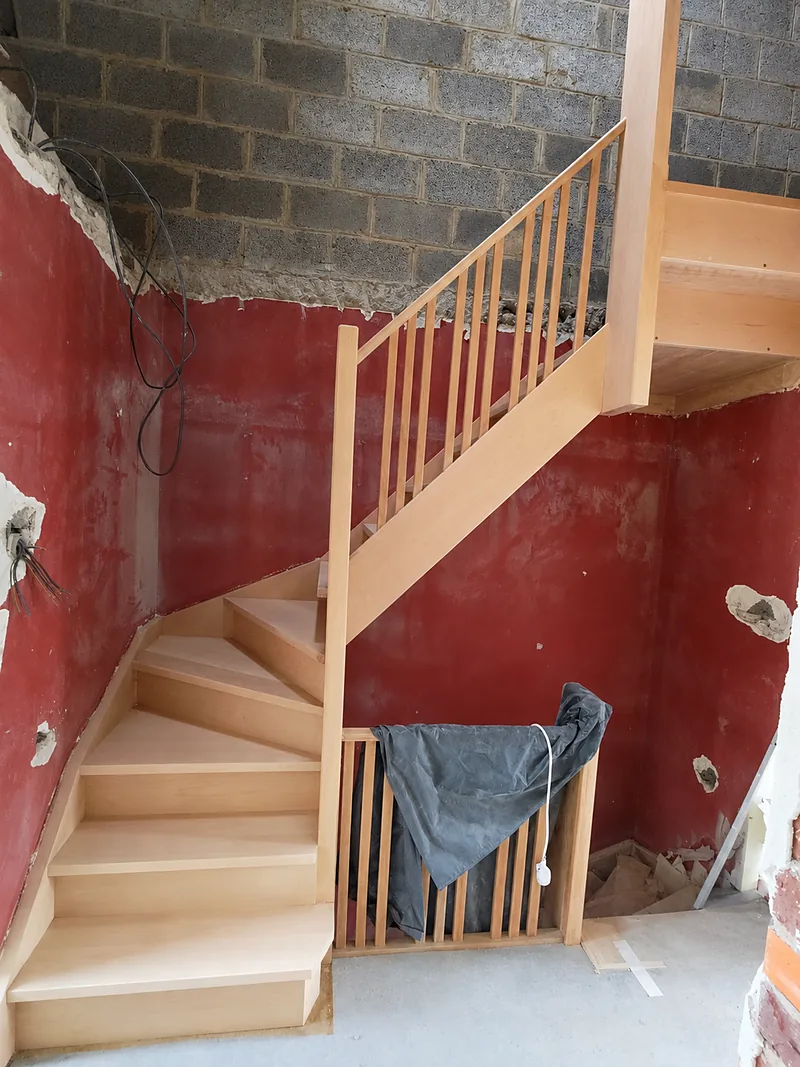 Escalier tournant en bois clair avec garde-corps à fuseaux, en cours de pose dans une maison en rénovation