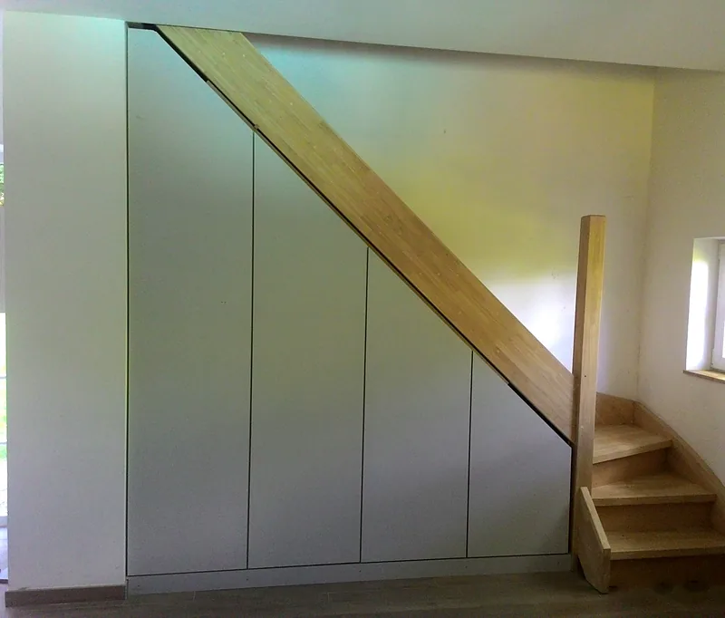 Placards sur mesure sous un escalier en bois, portes blanches fermées