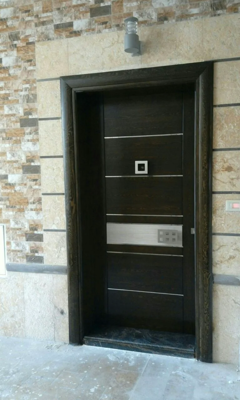 Porte d'entrée contemporaine en bois foncé à filets métalliques, dans une façade en pierre