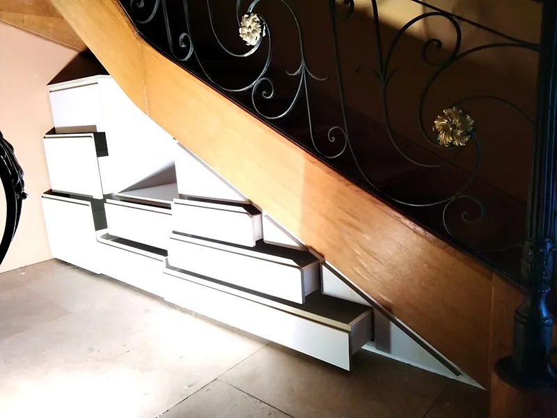 Tiroirs sur mesure en gradins sous un escalier à rampe en fer forgé