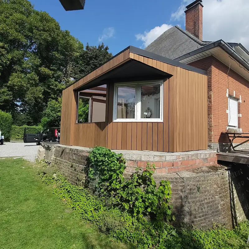 Véranda en bois adossée à une maison en briques, vue depuis le jardin